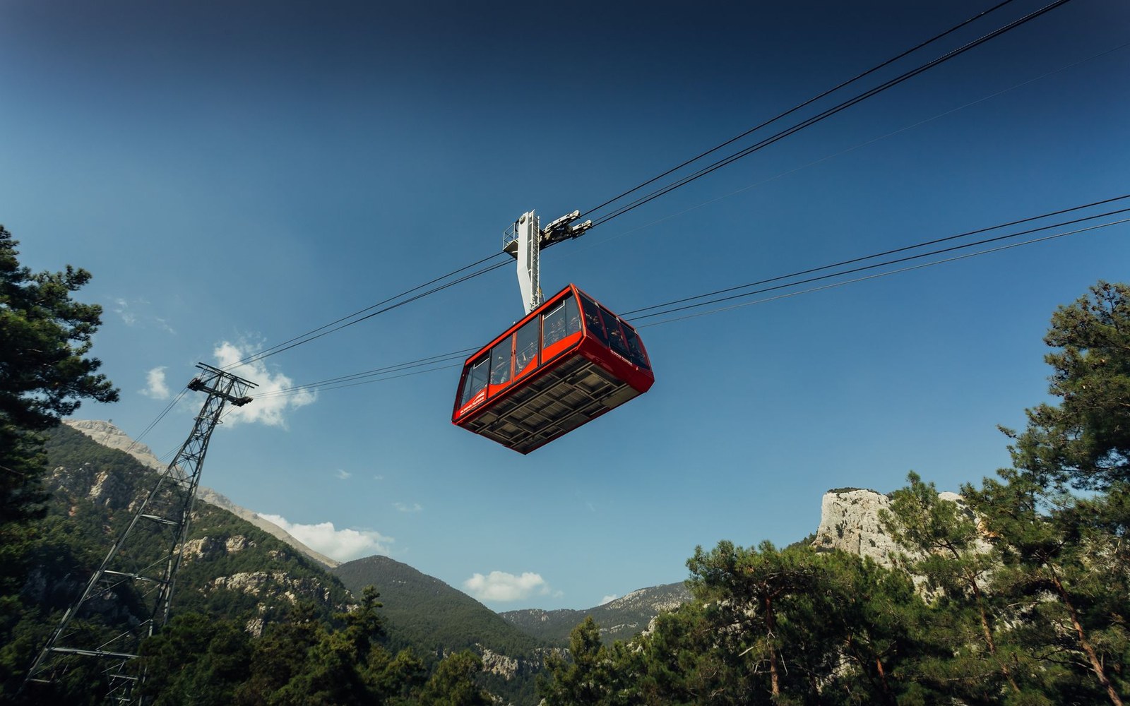 A cable-car pylon set against bare grey granite at high altitude, the cable running out of frame, no snow on the ground