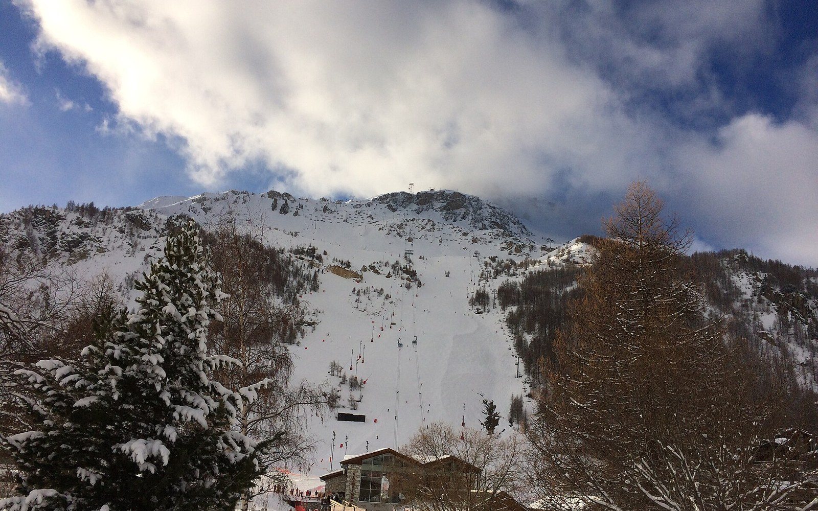 Snow-covered mountain slope with ski lift towers rising above a chalet building