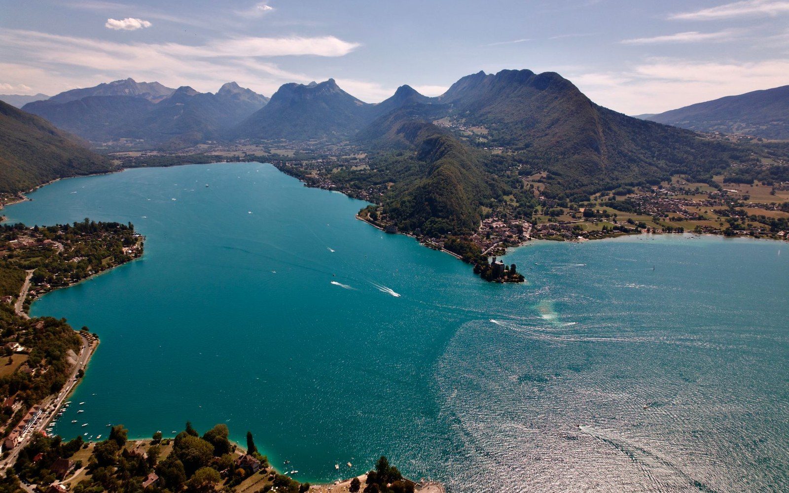 Aerial view of a turquoise alpine lake surrounded by forested mountains and lakeside villages
