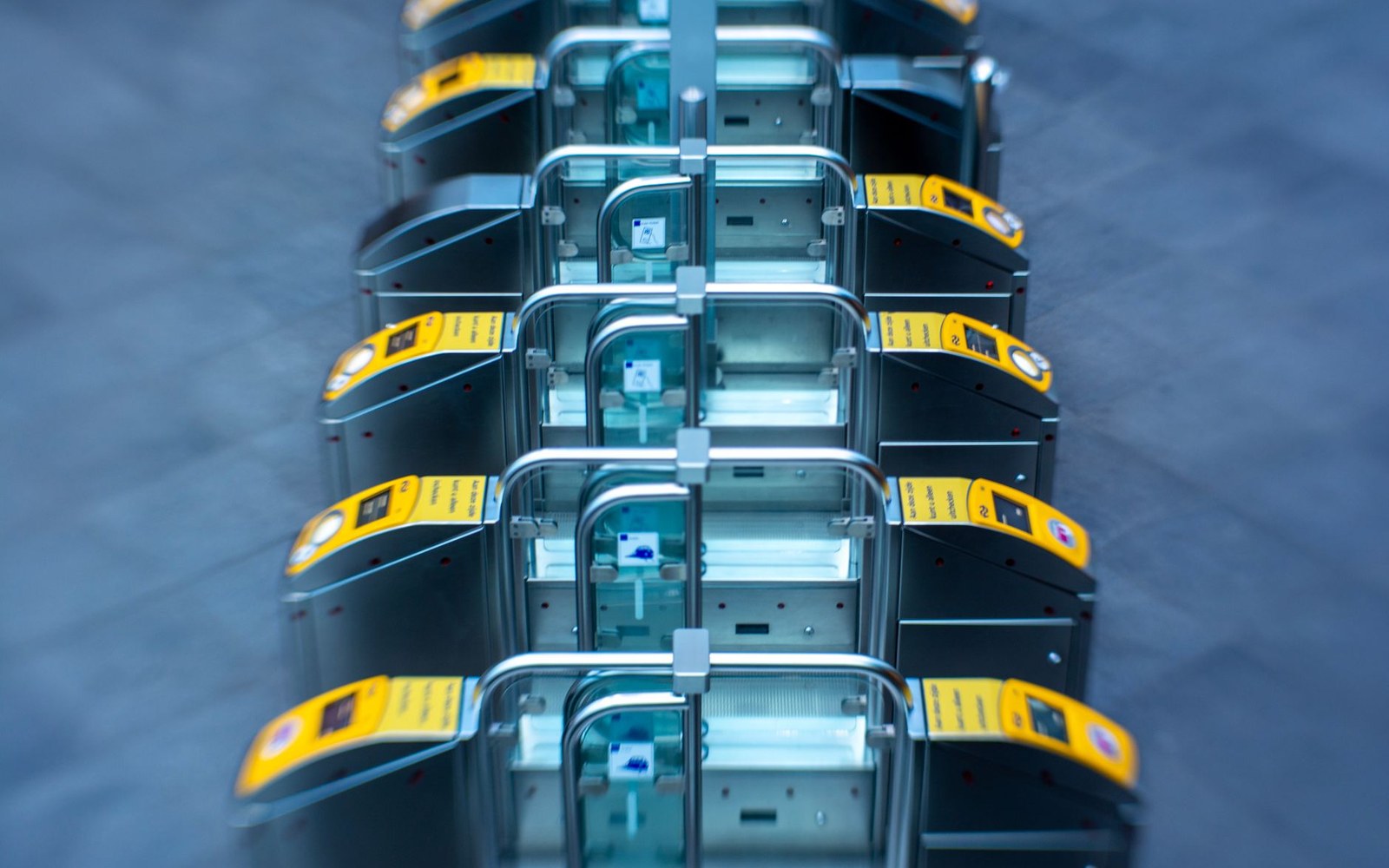 Rows of automated ticket barriers with yellow card readers line up in a station