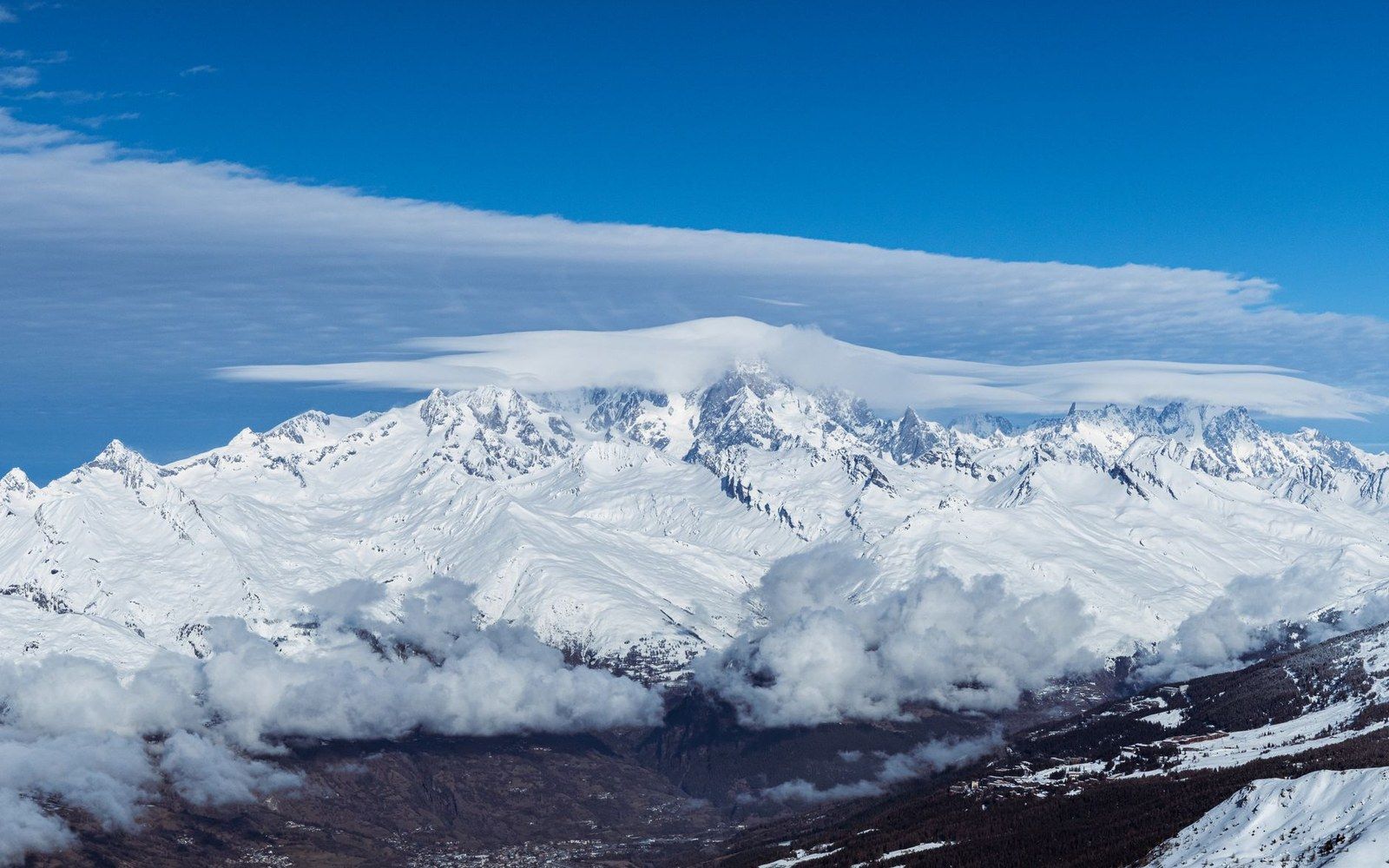 Snow-covered alpine peaks capped with lenticular clouds above a misty valley