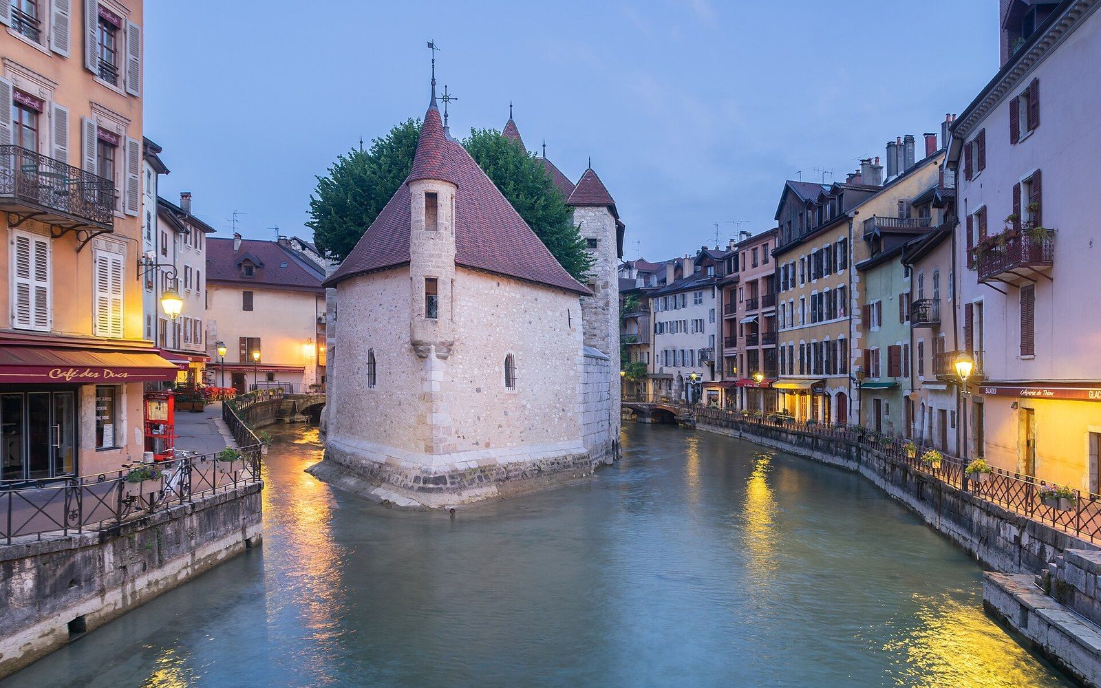 Annecy's old-town rooftops seen from above, the Palais de l'Isle on its island in the Thiou canal, the lake and the Semnoz ridge in the background