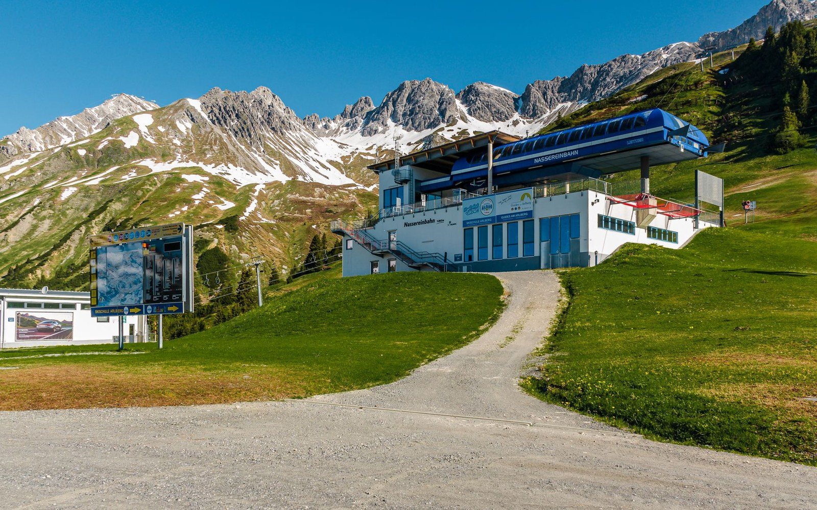 A ski-lift station's turnstile gates closed and unlit in summer, the empty loading bay beyond them, mountain visible through the open doors